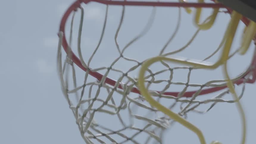 A boy is tossing a basketball into a net outside during the day