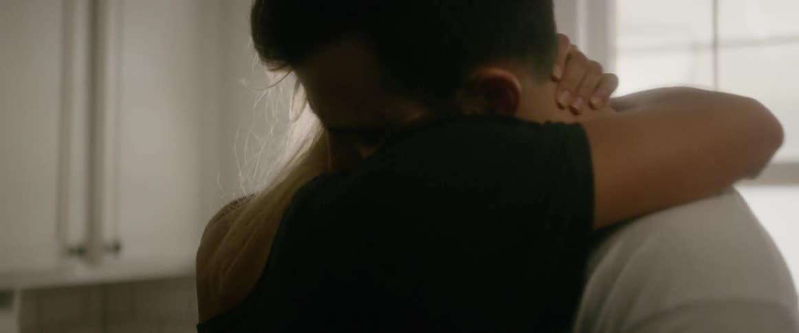 A woman is leaning in to embrace a man indoors during the day