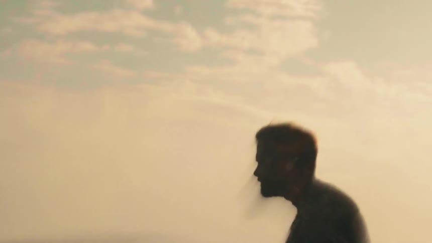 Man stands in the ocean then mounts his surfboard