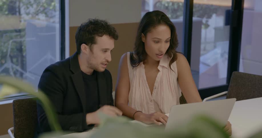 A man and woman sit side by side and work on a laptop