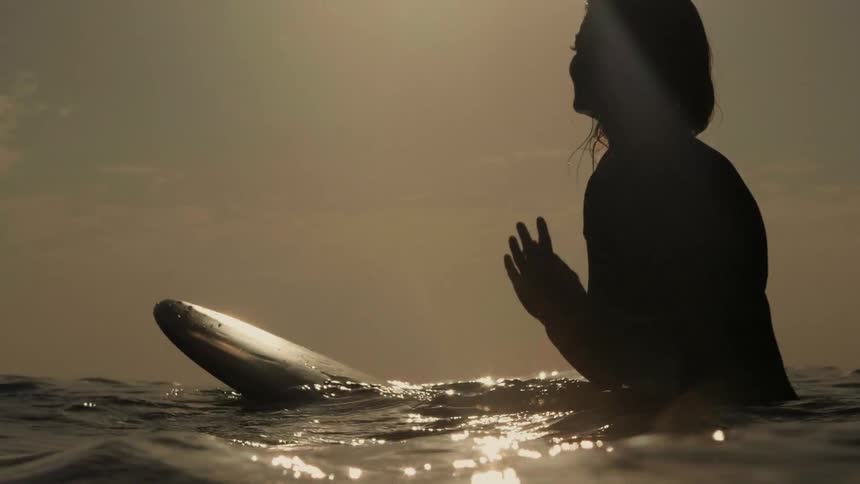 A surfer floats on the ocean at sunset