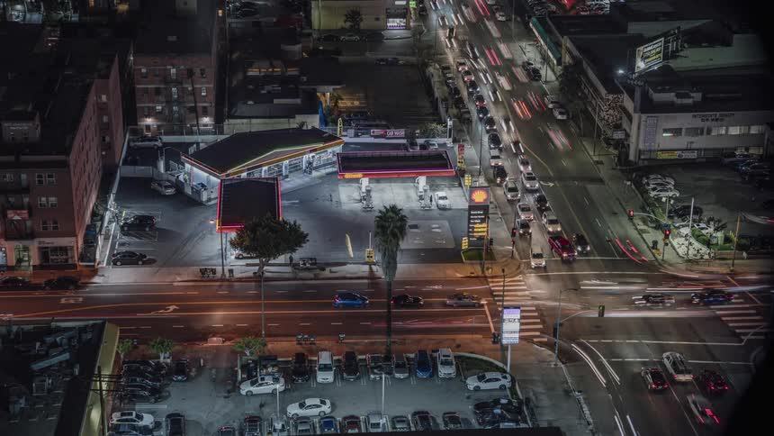 Traffic travels through a city intersection and a gas station at night
