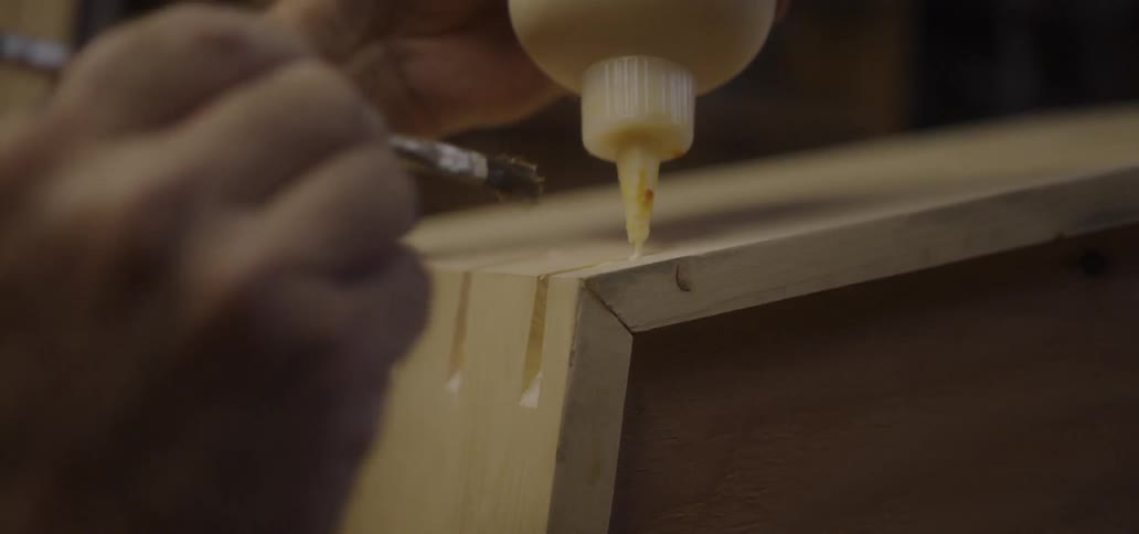 A person is applying glue to wood with a brush