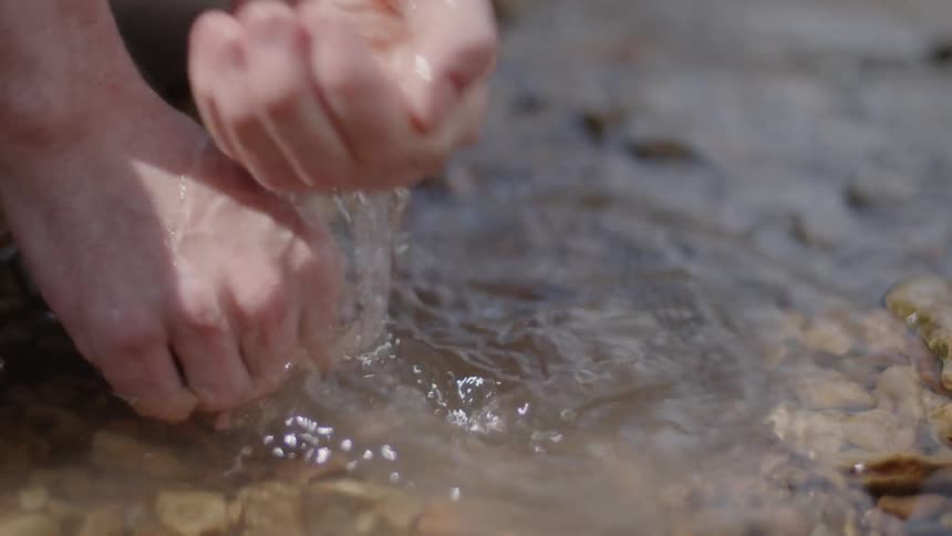 A person pours water over their hands from a stream
