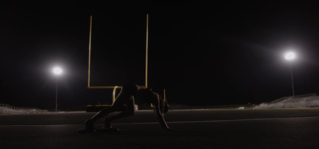 A runner stretches and crouches on an outdoor track at night