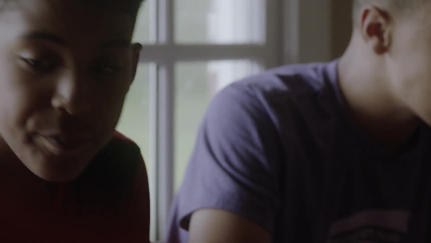Teenage boys are sitting at a table having a snack inside in daylight