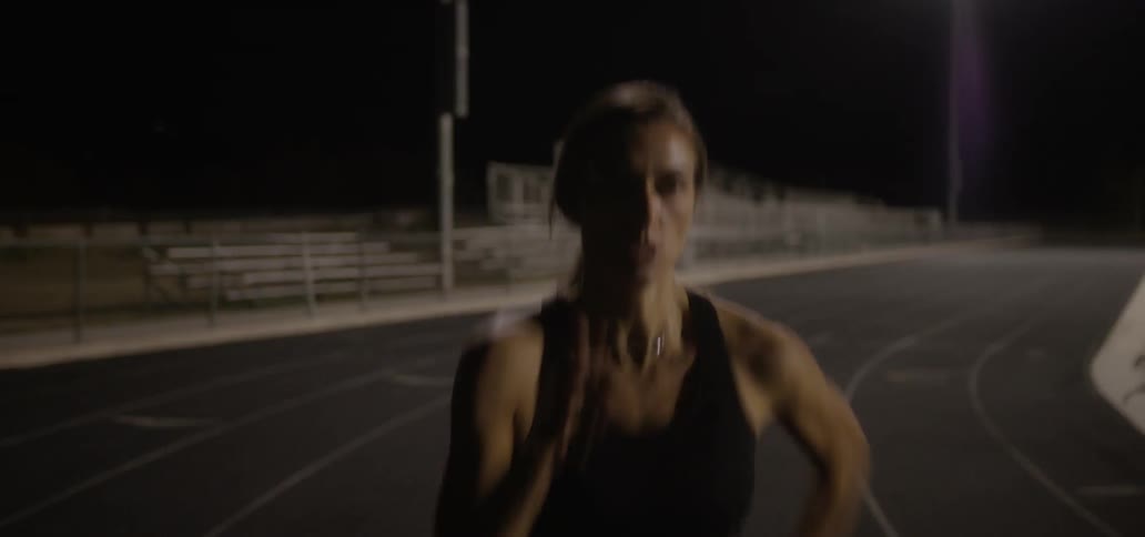 Woman in a sports bra jogs on a track at night