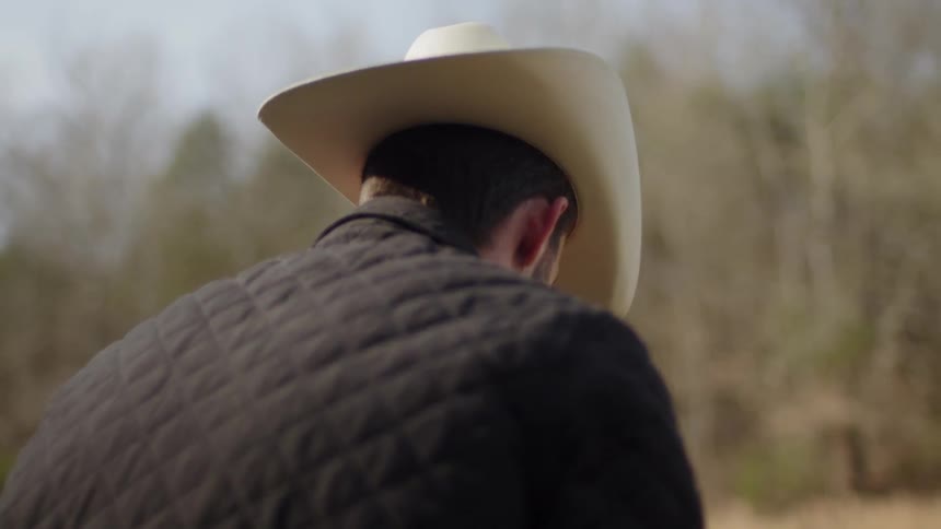 A man is leaning forward wearing a cowboy hat