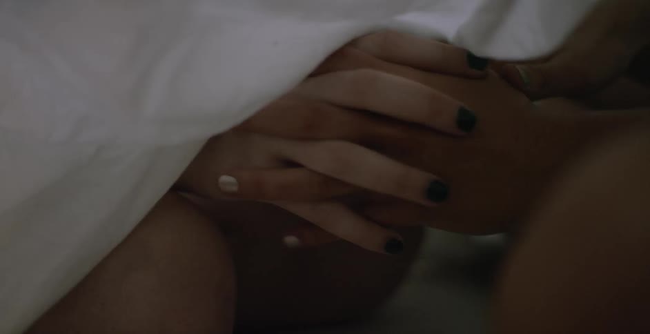 Two women hold hands beneath a blanket
