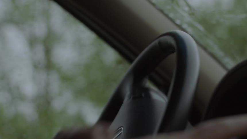 Person turns a steering wheel around in a car while windshield wipers move