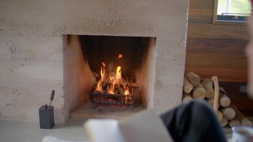 A man reads in front of a fire
