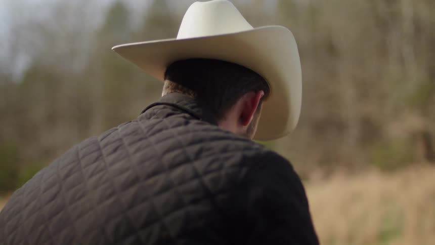 Man wearing a cowboy hat and quilted jacket looks towards the ground