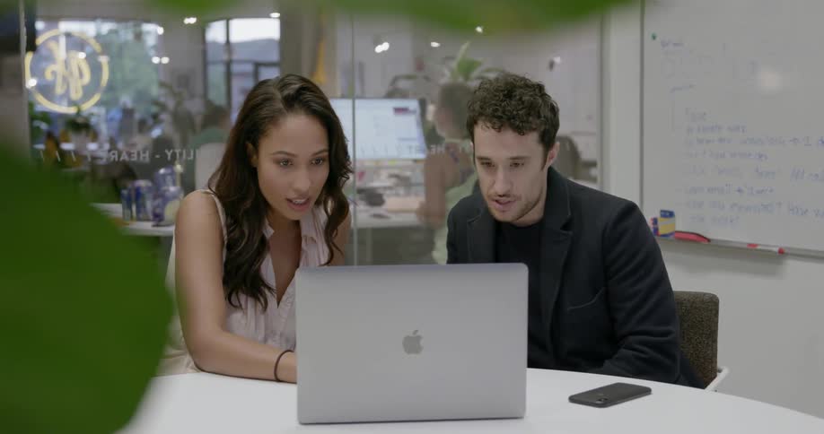 Two people sit in the conference room looking at a laptop together