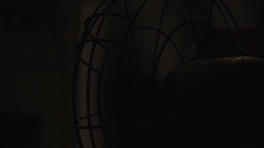 A table fan operates in a dark room