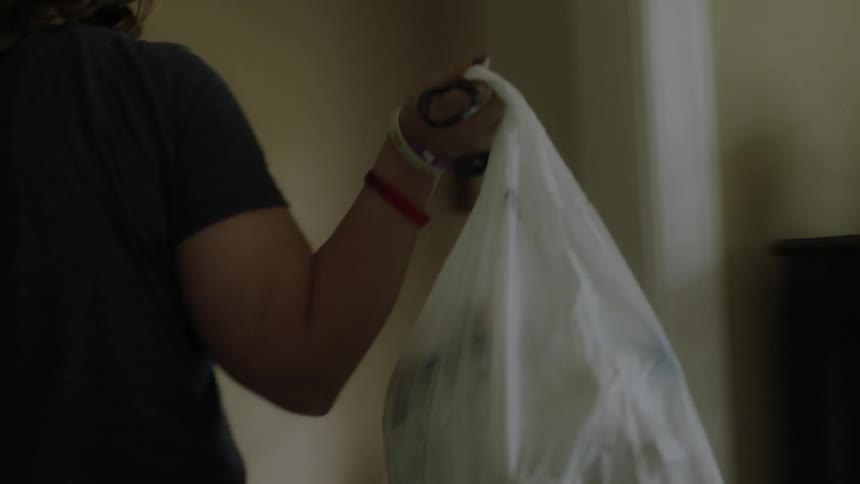 A woman is pulling a trash bag out of a canister and placing it in a pile inside in daylight