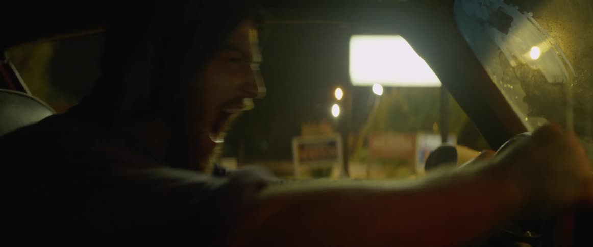 A man sits in a car and screams and bangs on the steering wheel