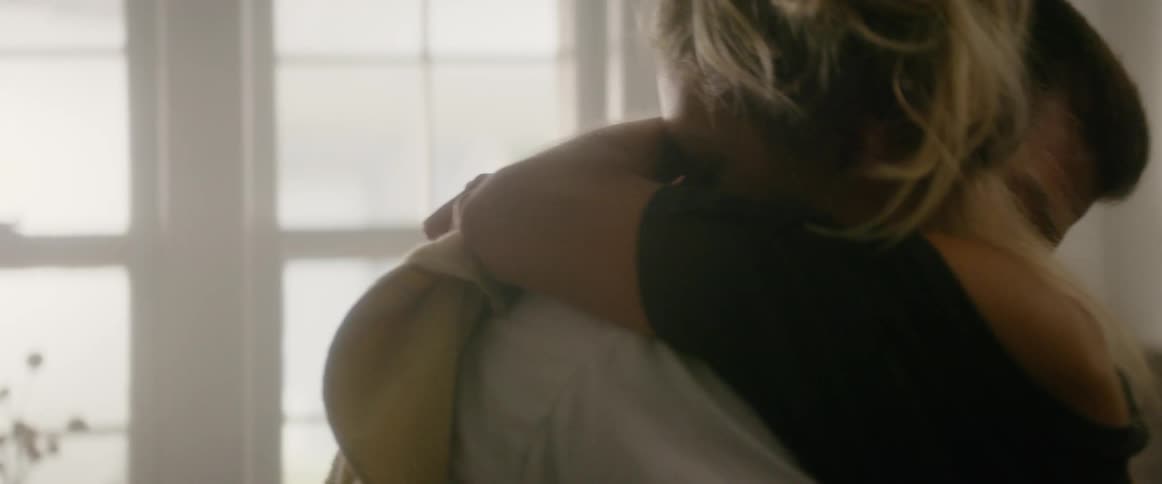A woman hugs a man by the window