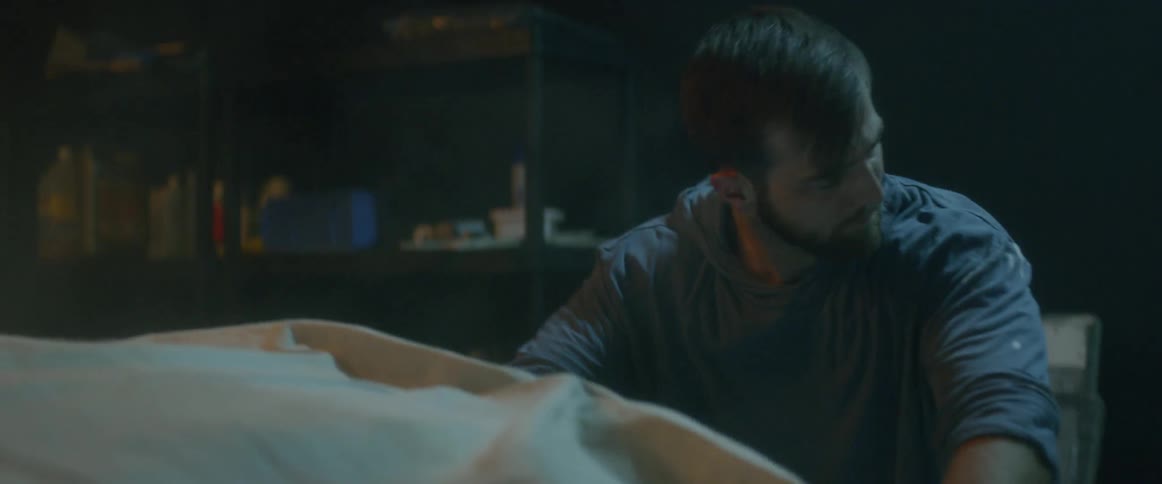 Dust rises as a man beats his hands against the cloth covering a car