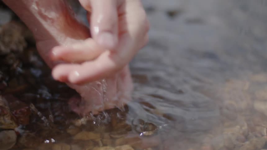 A person washes their hands in the stream