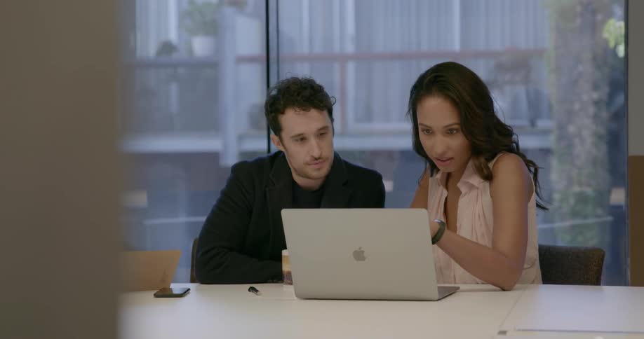 A man and woman are sitting at a conference table working in daylight