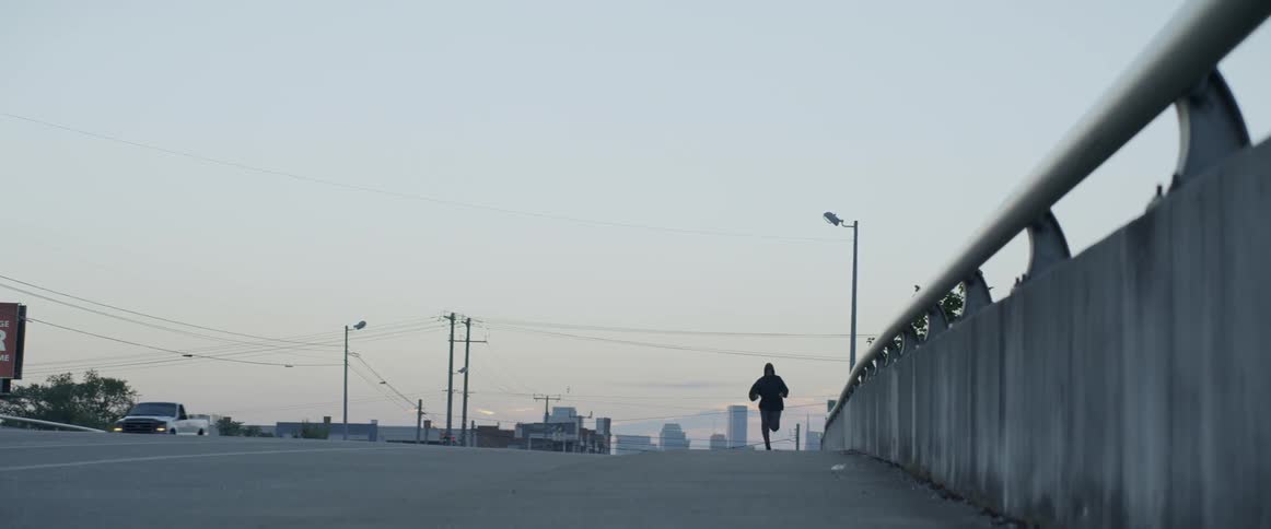Man jogs alongside a fence on a sunny day