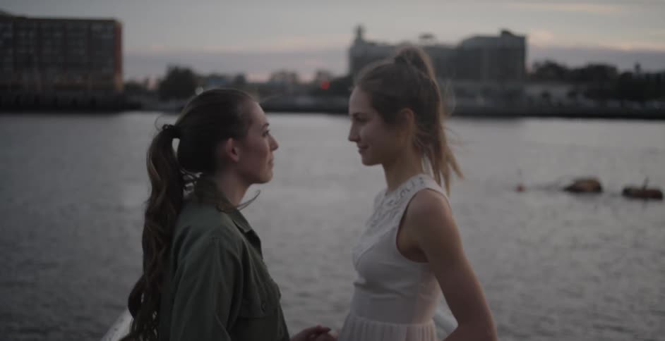 Women speak and hold hands by an urban river
