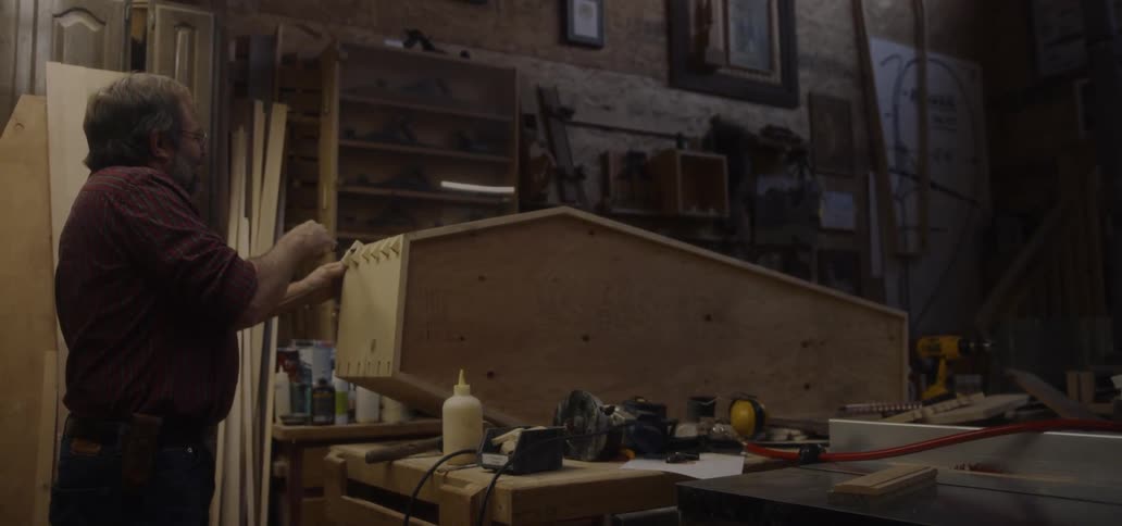 A man uses a saw on a wooden coffin in a workshop