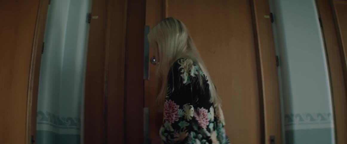A woman in a floral jacket opens a wooden front door to exit.