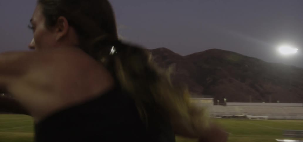 A woman jumps hurdles on a track at night