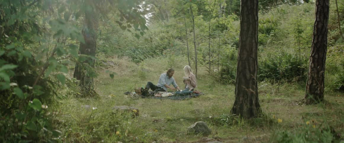 A young man and woman have a picnic in a quiet grassy forest.