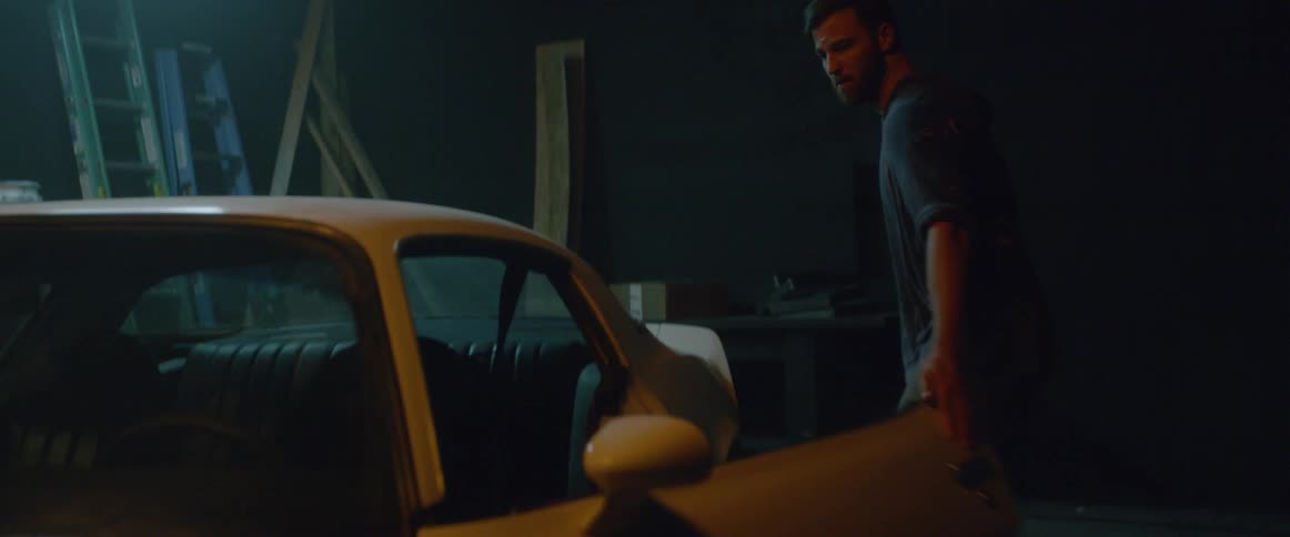 A man is removing a cover from a car in a shed in daylight