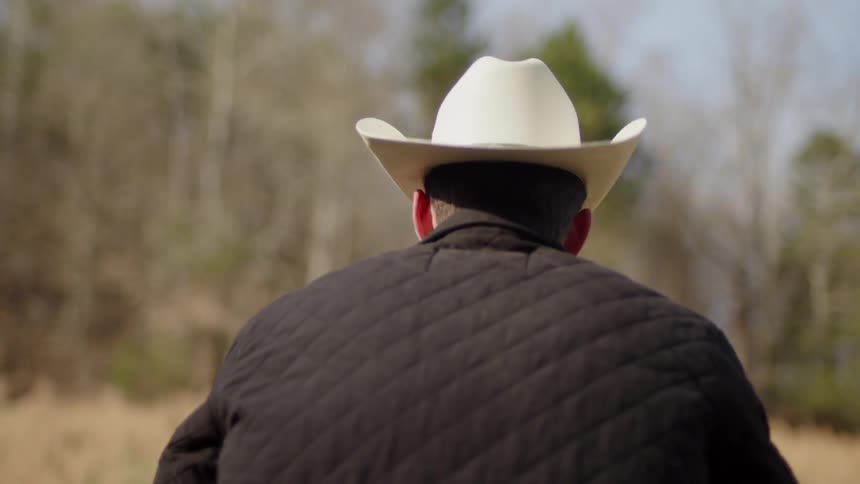 A man in a cowboy hat is standing in a clearing in the woods