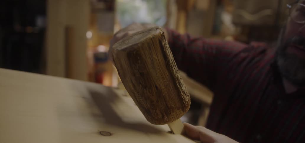 A carpenter hammers a piece of wood