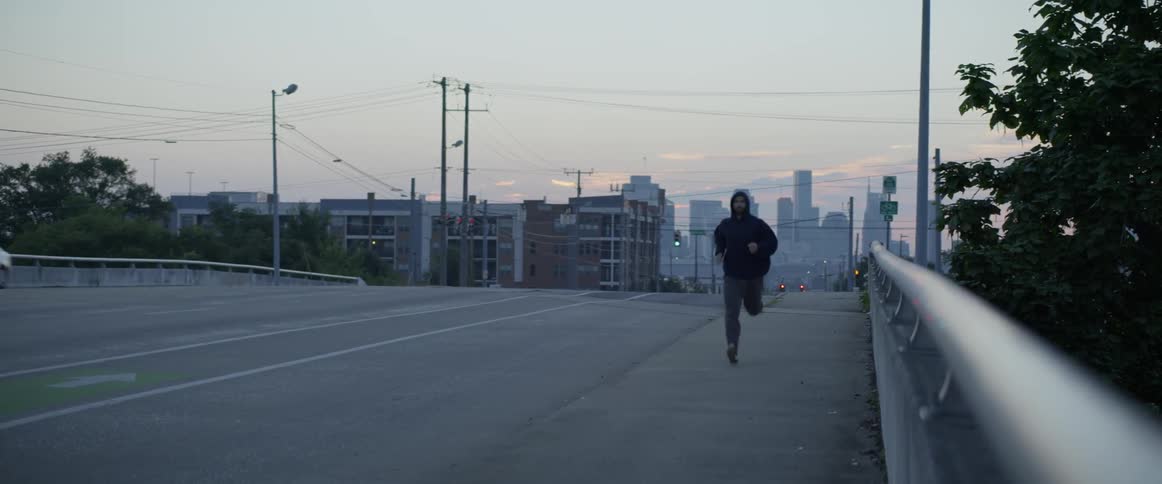 Man is jogging over bridge in city at dawn