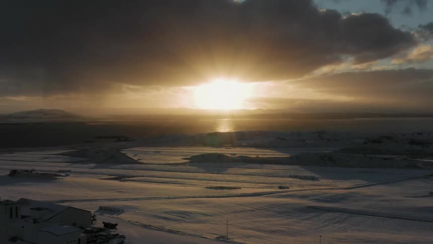 The sun is setting behind the dark clouds by the shore