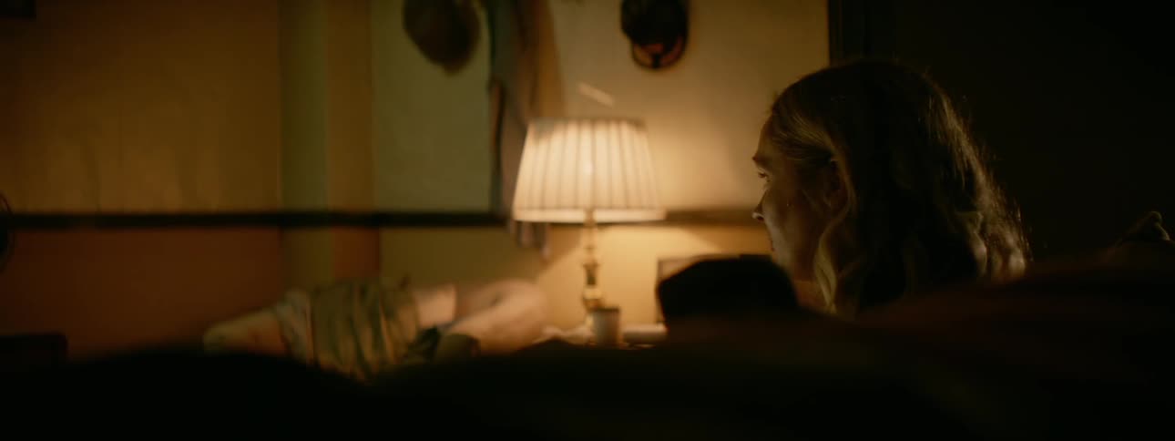 A woman sits near a lamp in a dark room
