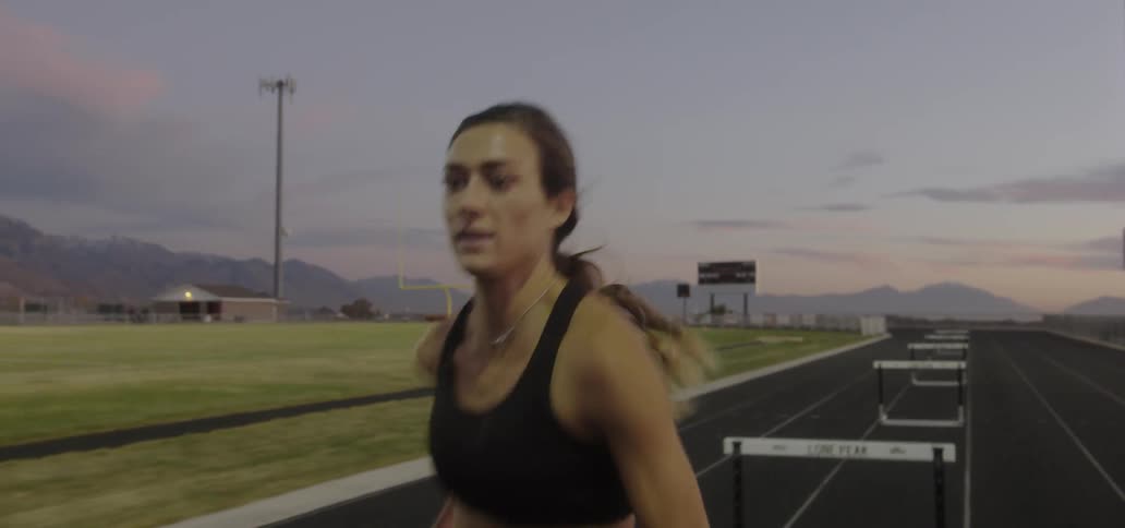 Woman running fast on track and jumping over hurdles