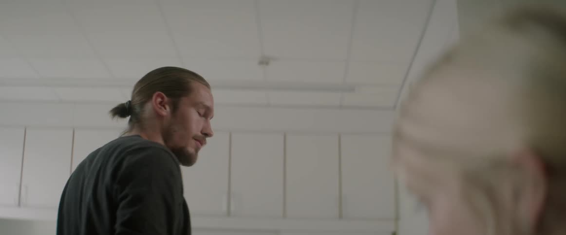 A young man talks to a blonde woman and walks away inside an office.
