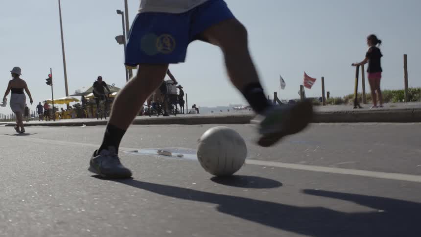 A person kicks the soccer ball along the shore road
