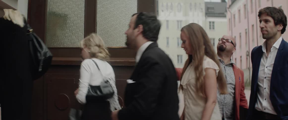 A group of smartly dressed people walks past a door into a building.