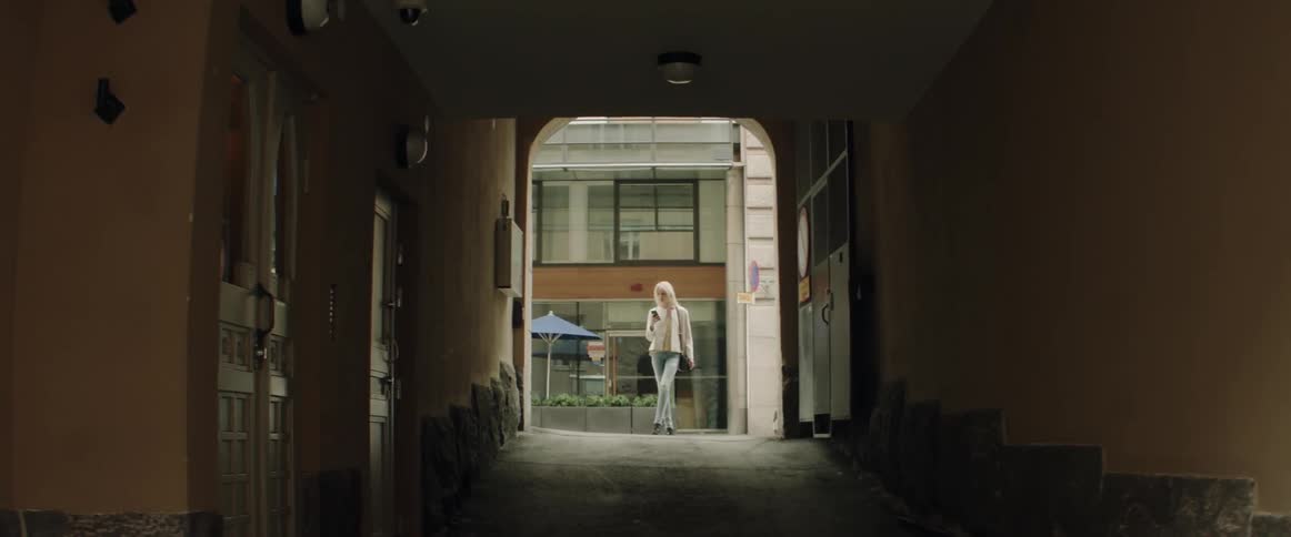 Woman walks down a street and then turns into large entry way