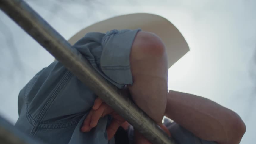 A cowboy leans against a railing on a sunny day