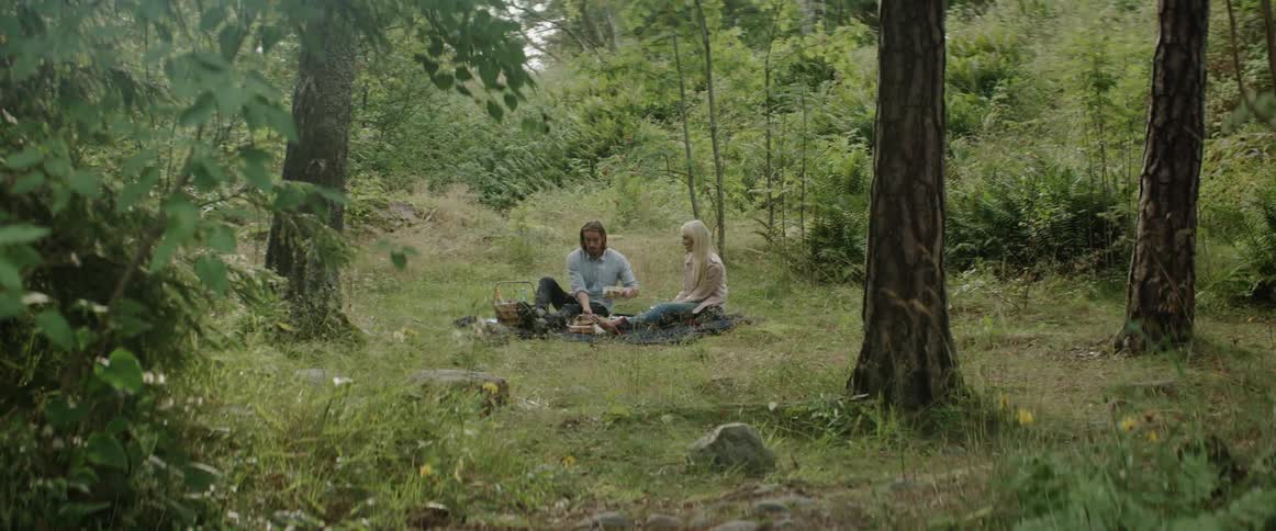 A man and woman have a picnic in the grass between the trees