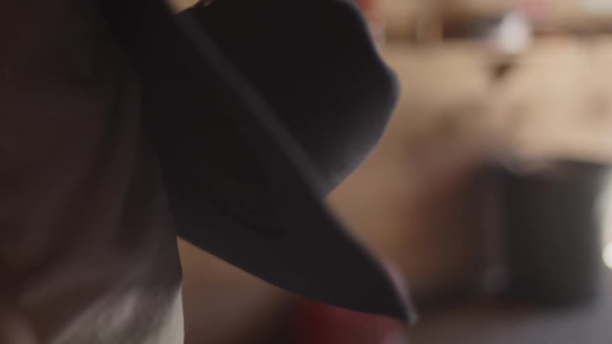 The man adjusts his cowboy hat in the barn