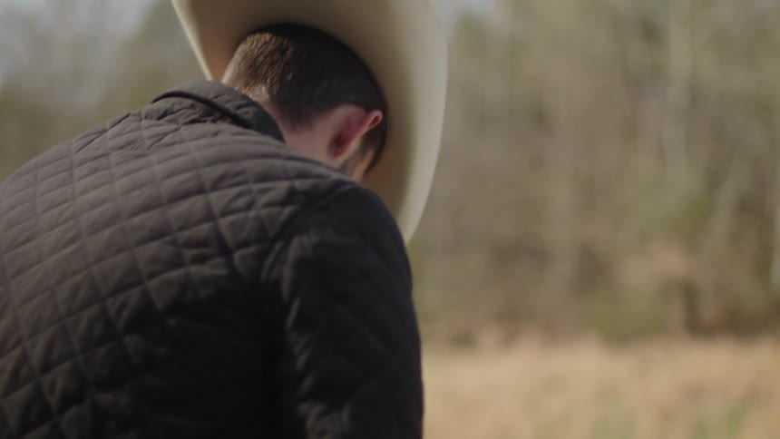 A rancher sits on a fence on a sunny day