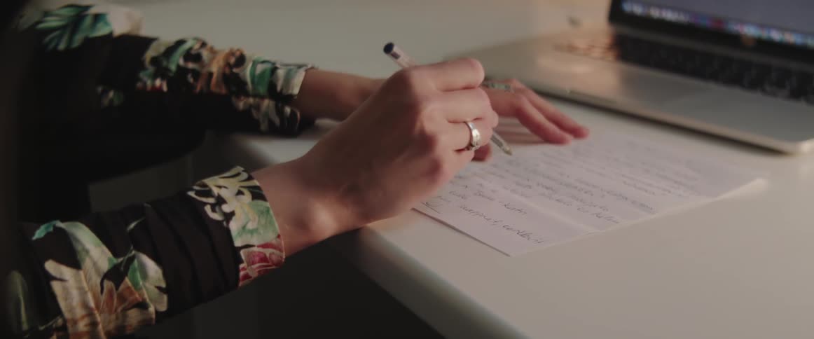 A woman writes notes on paper with a pen while working at home.