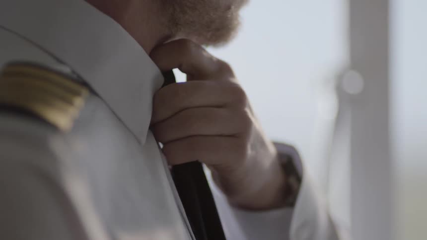 An airline pilot is adjusting his cuffs and ties as he prepares for his day