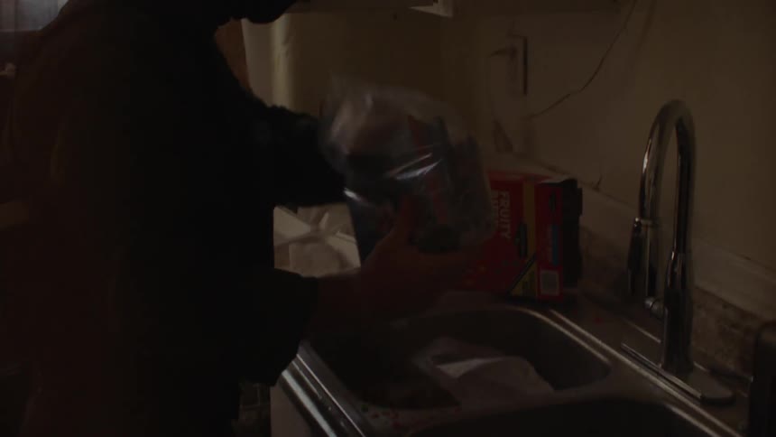 A police officer is searching through items in a kitchen in daylight