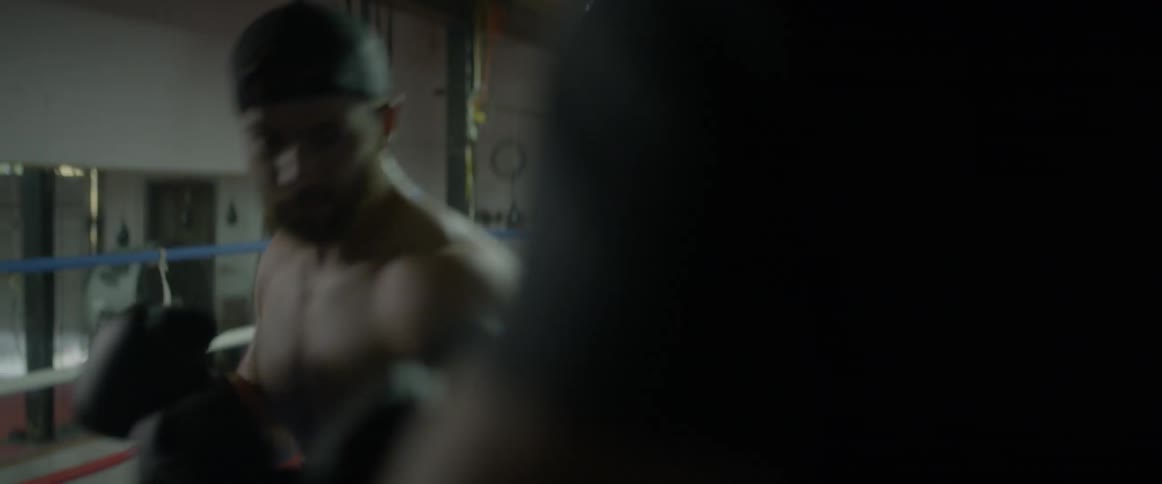 A fighter is trading blows with his trainer inside a boxing ring in a gym