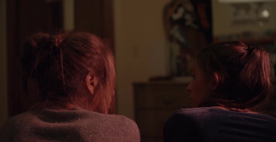 Two women sitting on a bed are turning to look at each other